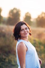 Portrait of happy pregnant woman in park at sunset with warm backlight in the background