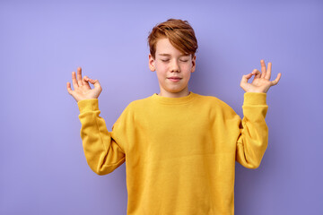 Portrait of young teenage boy keep calm, meditating, isolated on purple studio background. Kid in...