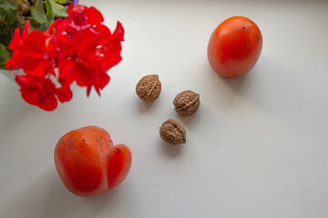 geranium two persimmons three walnuts on a white background. view from above