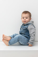 portrait of a sitting toddler on a white background, a boy 1-2 years old in jeans looks at the camera, a cute satisfied child