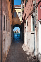 Fototapeta na wymiar Narrow street in Giudecca, island in Venetian lagoon. Historic houses form an arch passageway leading towards canal and historic houses on the other side across the water.