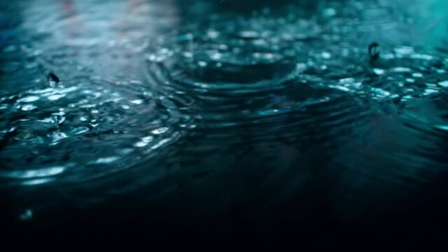 Rain drops falling into puddle at night