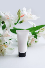 moisturizer in a white tube with a black cap on a background of alstroemeria close-up