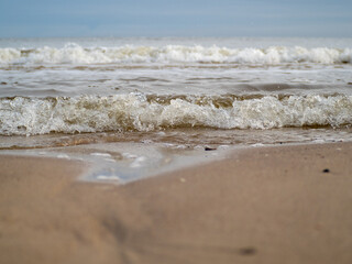 Wave with white foamy coastline beach. Sandy shore.