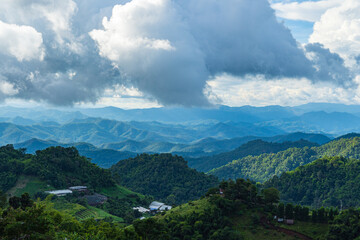 Fototapeta premium Rain clouds are moving towards the green forested mountain ranges in the evening of northern Thailand.