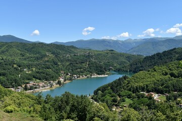 Fototapeta na wymiar Gramolazzo lake in Lunigiana, with boats and reflections, blue sky and no clouds, Apuan Alps in the background