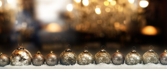 Line of golden shiny christmas balls in snow in front of abstract background with festive bokeh...