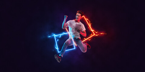 Art collage. Young excited man with tablet jumping isolated on dark background with neoned geometric figure