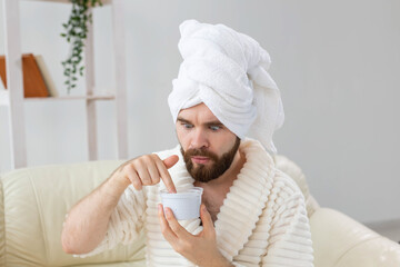 Portrait of man applying effective cream on his facial skin. Spa at home, body and skin care for male concept.