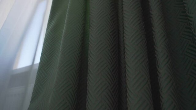 Green colored dense fabric drape hanging on window cornice in living room low angle shot