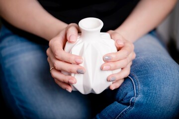 Female hands holding white ceramic vase. Manicure with pink and gray color nail polish