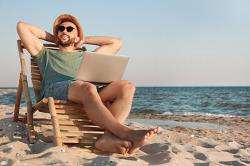 Man with laptop relaxing in deck chair on beach - Powered by Adobe