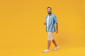 Full body young smiling happy cheerful satisfied caucasian man 20s wearing blue shirt white t-shirt walking going stroll isolated on plain yellow background studio portrait. People lifestyle concept.