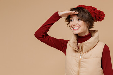 Young smiling happy caucasian woman 20s wears red turtleneck vest beret hold hand at forehead look far away distance isolated on plain pastel beige background studio portrait People lifestyle concept