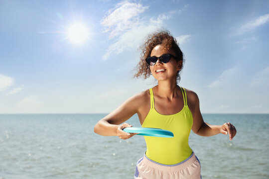 Happy African American woman throwing flying disk at beach on sunny day
