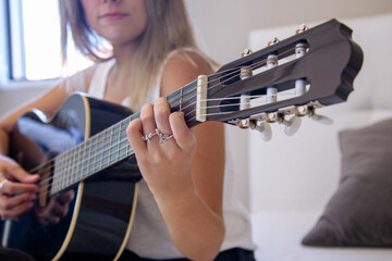 Chica tocando la guitarra en su habitación. Mujer mirando su guitarra española mientras toca en su casa. Mujer practicando un hobbie. Estilo de vida