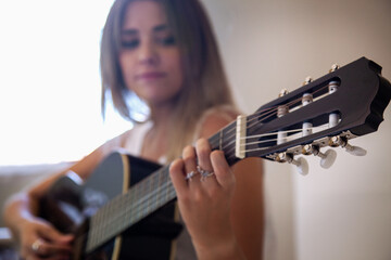 Chica tocando la guitarra en su habitación. Mujer mirando su guitarra española mientras toca en...