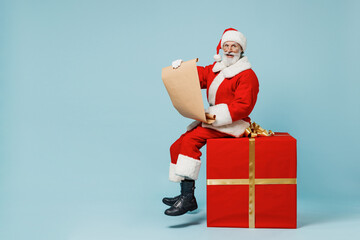 Full size old Santa Claus man in Christmas hat red suit clothes sitting on big gift present box read letter isolated on plain blue background studio Happy New Year 2022 merry ho x-mas holiday concept.