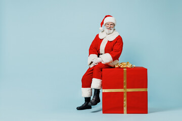 Full body old Santa Claus man in Christmas hat red suit clothes sitting on big gift present box isolated on plain blue background studio Happy New Year 2022 celebration merry ho x-mas holiday concept