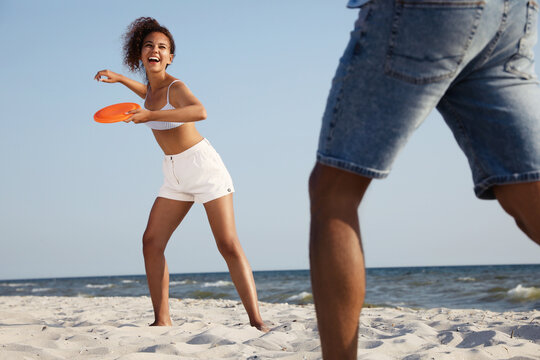 Couple playing with flying disk at beach on sunny day