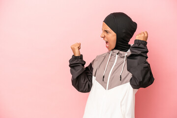 Young Arab woman with sport burqa isolated on pink background raising fist after a victory, winner concept.