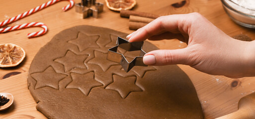 Closeup of Woman's hand cutting homemade gingerbread cookies on wooden background. Christmas baking concept.