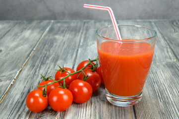 A glass of tomato juice with a straw. A bunch of bush tomatoes lies nearby