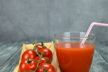 A glass of tomato juice with a straw and a bunch of bush tomatoes lies on a wooden tray