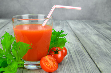 A glass of tomato juice with a straw. Parsley and tomato leaves are laid out around
