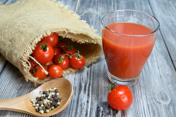 A glass of tomato juice, allspice on a wooden spoon and tomatoes wrapped in a coarse linen cloth