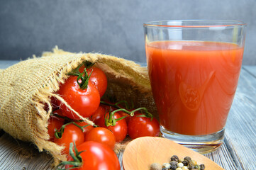 A glass of tomato juice, allspice on a wooden spoon and tomatoes wrapped in a coarse linen cloth
