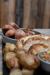 Traditional asado criollo plate. Closeup view of chorizos, pork sausages, grilled sweetbreads, potatoes, bread and criolla sauce on the wooden table.