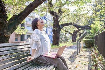 Fototapeta premium 公園のベンチに座って伸びをするノートパソコンを持った日本人女性