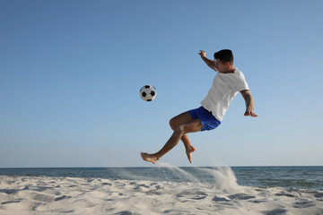 Man kicking football ball on beach near sea