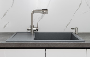 Gray kitchen sink with silver water tap and integrated detergent dispenser against marble...