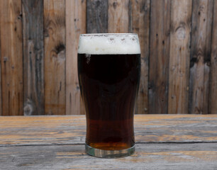 Brew. Closeup view of a dark beer with perfect foam on the the wooden table.