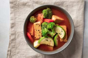Tofu soup with broccoli, zucchini, bell pepper in dark bowl. Asian cuisine, vegan food concept. closeup