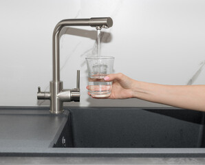 Woman pouring filtered purified water from tap into glass in kitchen. clean water and healthy life...