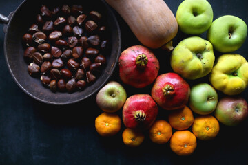 Pan with chestnuts, butternut squash and various fruit on dark background. Flat lay.