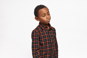 Horizontal studio picture of upset cute dark-skinned boy in plaid red and black shirt looking aside...