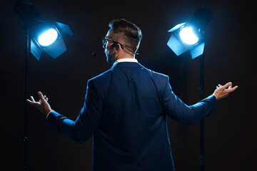 Motivational speaker with headset performing on stage, back view - obrazy, fototapety, plakaty