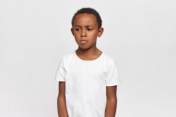 Angry, indulgent African kid, standing at studio isolated on white background with blank copy space...