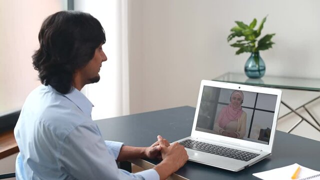 Back view multiracial middle-eastern man using computer app for video meeting with female friend or employee wearing hijab, guy using laptop, talking online with islamic woman. Video call