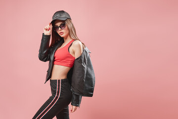 nice looking teenage girl in sunglasses in black cap posing while standing on pink background