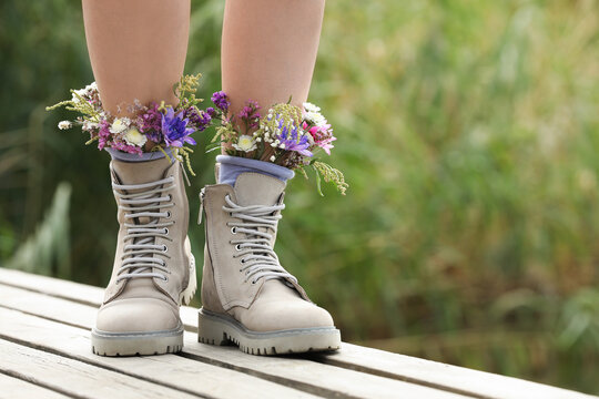 Woman standing on wooden pier with flowers in socks outdoors, closeup. Space for text