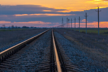 Fototapeta na wymiar Railroad track during sunset. Power line running along the railway.