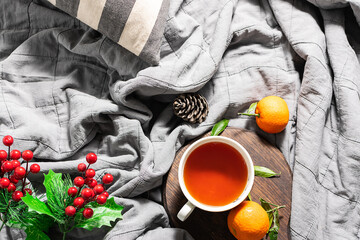 Cozy interior with cup of tea, candles, tangerines and Christmas decorations on grey plaid top view. Hygge style Christmas composition.
