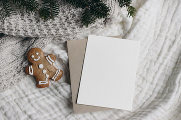 Christmas still life. Blank greeting card, invitation mockup with craft envelope.,Gingerbread man cookie and fir tree branches. White muslin table cloth, throw. Flatlay, top view. Winter holiday.
