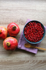 Bowl filled with pomegranate seeds and pomegranate fruit on a table. Flat lay.