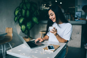 Positive Asian woman with cup of coffee browsing laptop